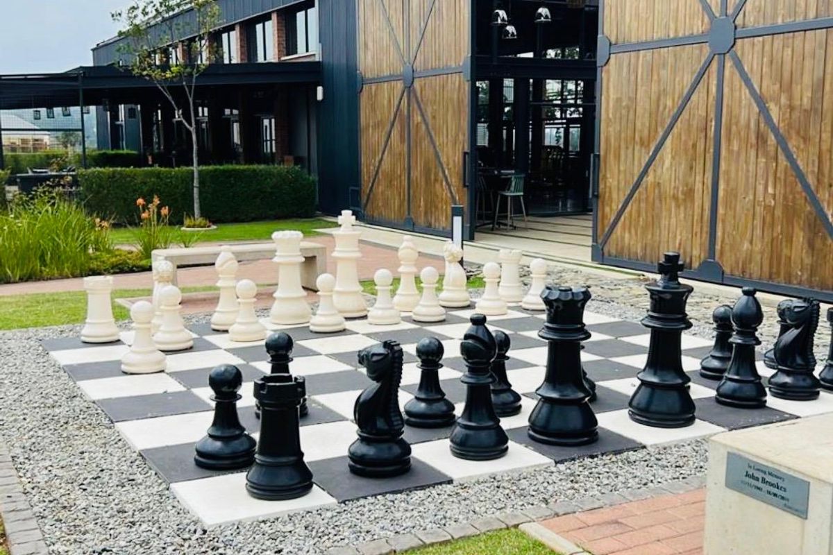 A well-maintained outdoor area featuring a large garden chess set, paved patio, and modern industrial-style building facade with large sliding wooden doors.