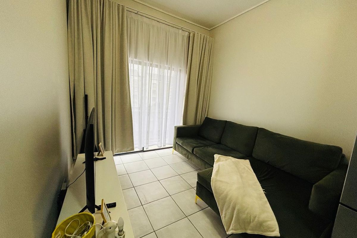 A compact living room featuring tiled flooring and a large sliding glass door with floor-to-ceiling curtains, providing access to an outdoor area.