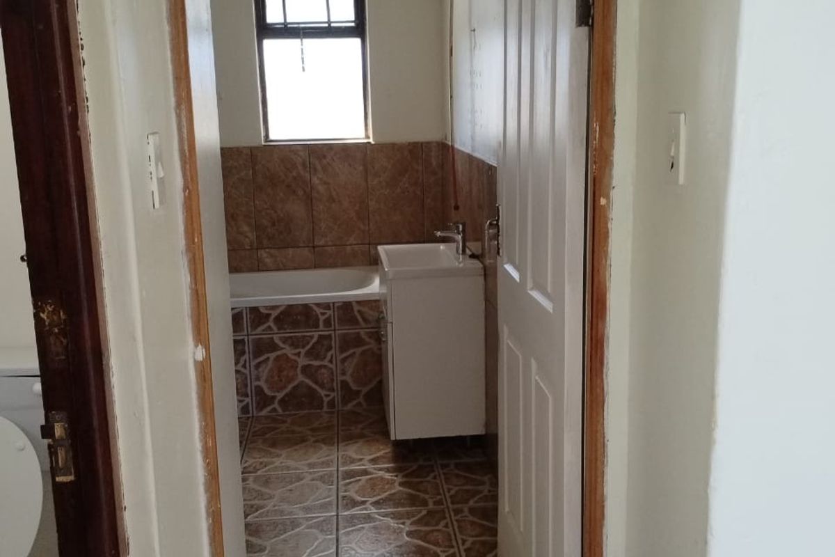 A functional bathroom featuring a bathtub, vanity basin, and tiled finishes, currently requiring cosmetic updates and repairs to the door frame.