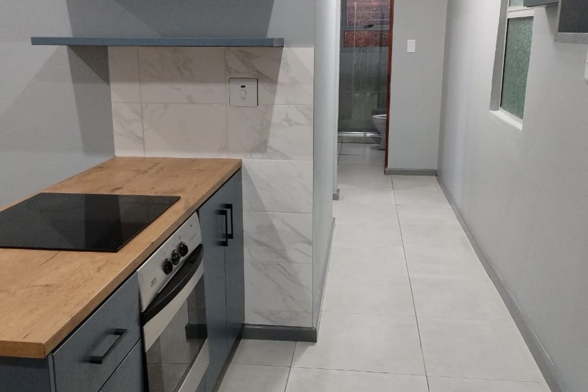Modern kitchen area featuring blue cabinetry, wooden countertops, built-in oven and hob, and neutral tiled flooring, leading to a bathroom area.