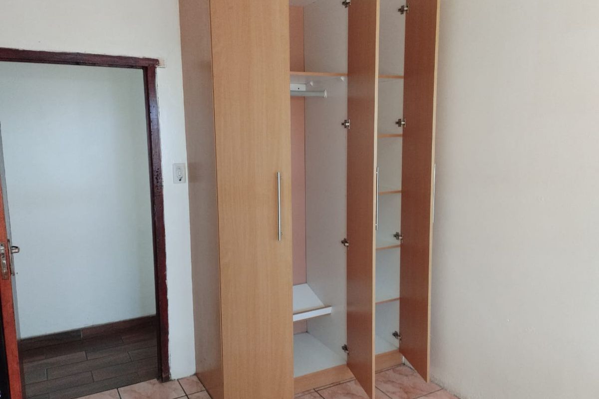 A bedroom featuring a built-in wooden wardrobe and tiled flooring, providing a functional storage solution in a neutral space.