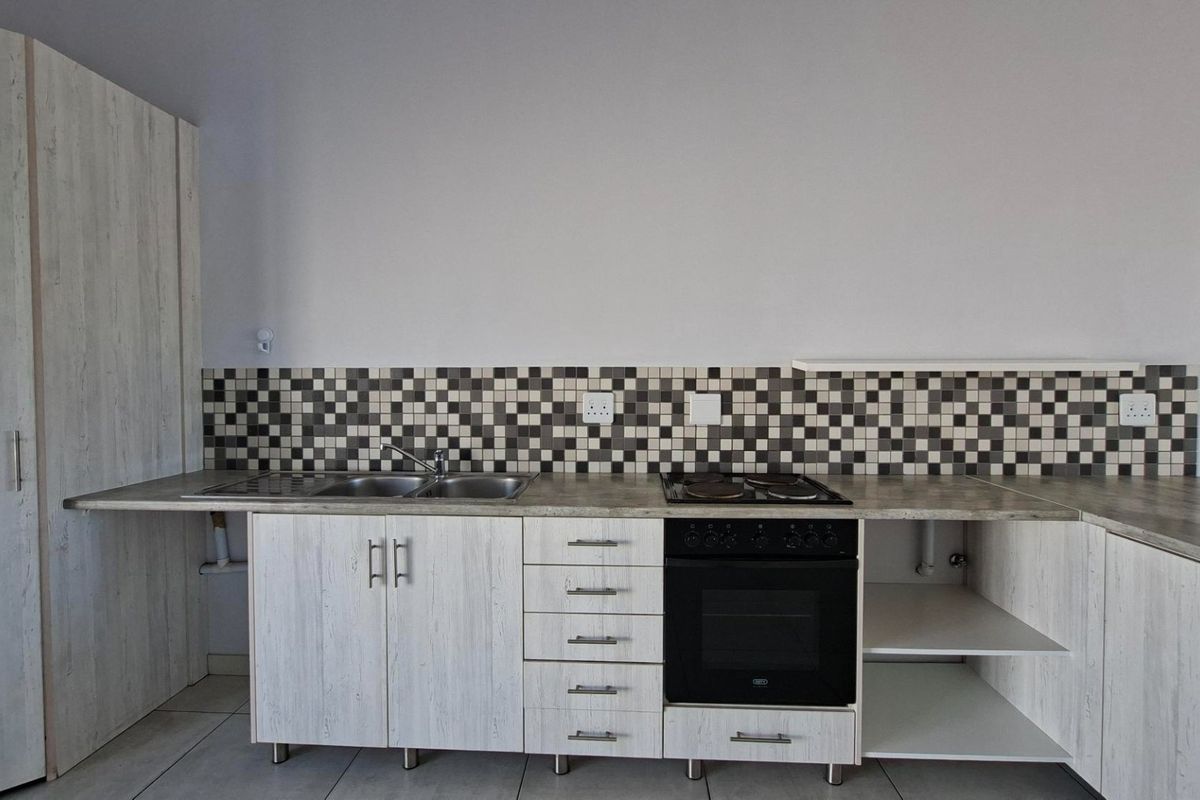 A clean, functional kitchen featuring light wood-grain cabinetry, a mosaic tile backsplash, built-in oven, electric hob, and a stainless steel double sink.