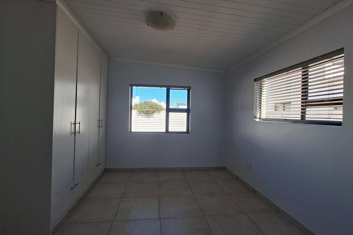 A bright, empty bedroom featuring neutral tiled flooring, built-in cupboards, and venetian blinds on the windows.