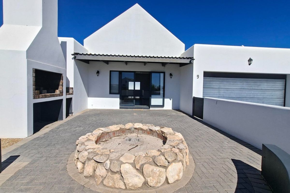 Rear exterior view featuring a paved patio, built-in braai area, and a stone fire pit, providing a functional outdoor entertainment space.