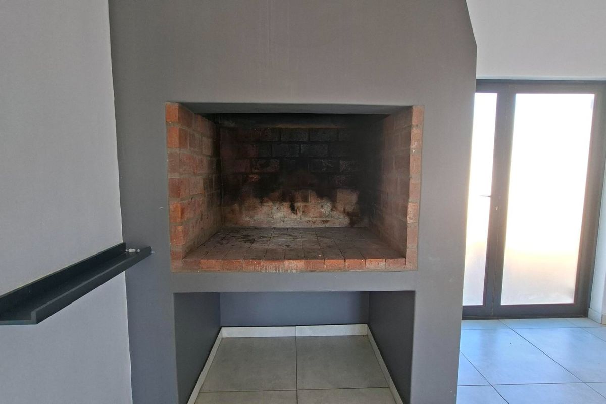 An empty living area featuring a built-in brick fireplace with a dark grey surround and tiled flooring, leading to a glass sliding door.
