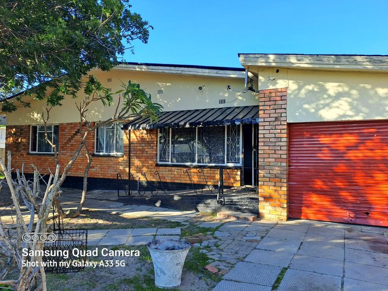Front elevation of a single-story brick house featuring a roller garage door, metal security bars on windows, and a paved driveway area.