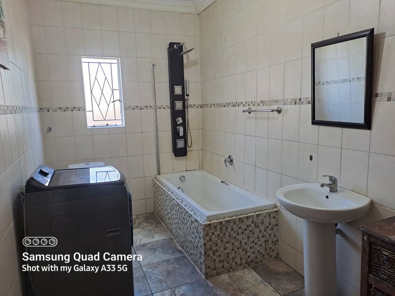 A functional bathroom featuring a pedestal basin, built-in bathtub with a modern shower panel, and fully tiled walls and flooring.