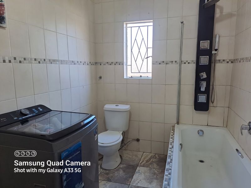 A functional bathroom featuring a built-in bathtub, wall-mounted shower panel, and toilet, finished with tiled walls and flooring.