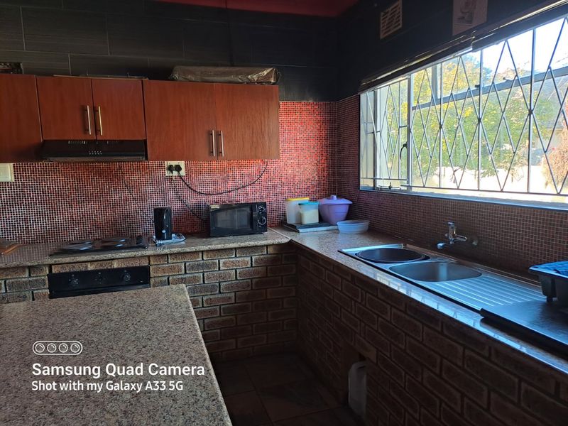 Kitchen featuring brick base cabinetry, granite countertops, mosaic tile backsplash, and built-in cooking appliances with security bars on the window.