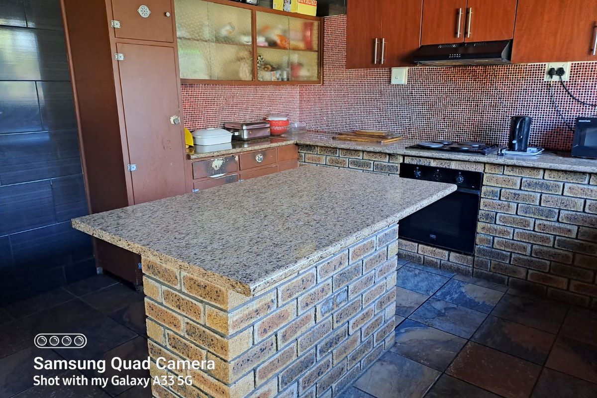 Kitchen featuring a brick island with granite countertop, built-in oven, gas hob, extractor fan, and tiled splashback with slate flooring.