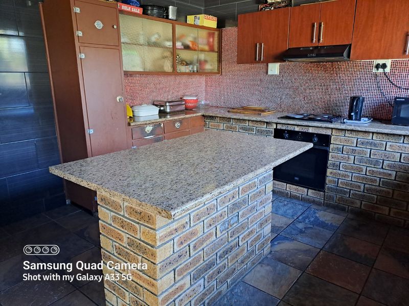 Kitchen featuring a brick island with granite countertop, built-in oven, gas hob, extractor fan, and tiled splashback with slate flooring.