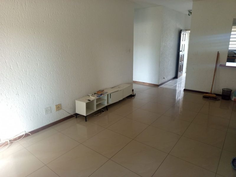 A spacious, empty living area featuring neutral tiled flooring and textured walls, providing a blank canvas for interior design.