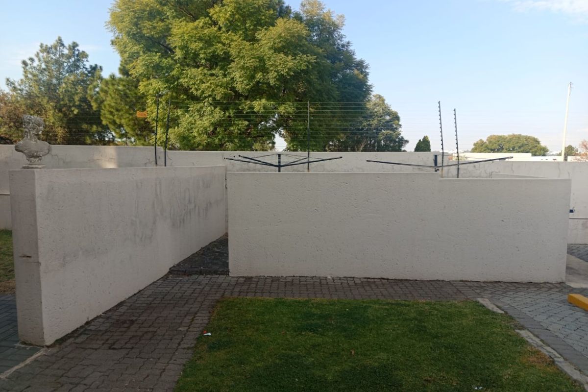 A private rear courtyard area featuring paved pathways, a small lawn, and perimeter boundary walls equipped with electric fencing.