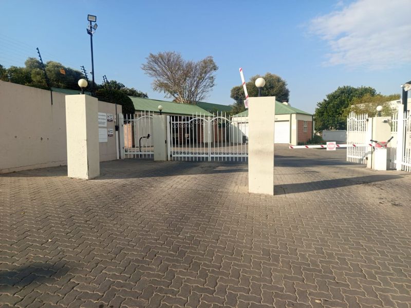 Secure gated entrance to the apartment complex featuring paved driveway, boom gate access, and perimeter electric fencing.