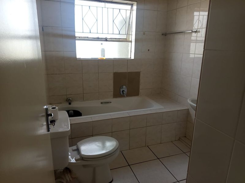 A dated bathroom featuring a built-in bathtub, toilet, and washbasin with tiled walls and flooring, requiring cosmetic updates to modernize the space.