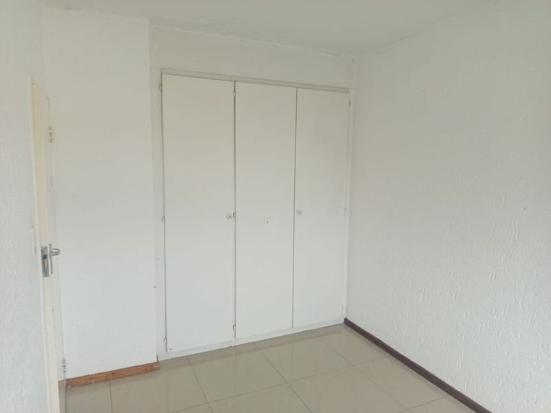An empty bedroom featuring tiled flooring and a built-in wardrobe with white doors.