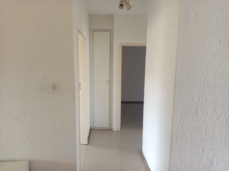 A vacant hallway featuring tiled flooring, textured walls, and a built-in storage cupboard, providing access to adjacent rooms.