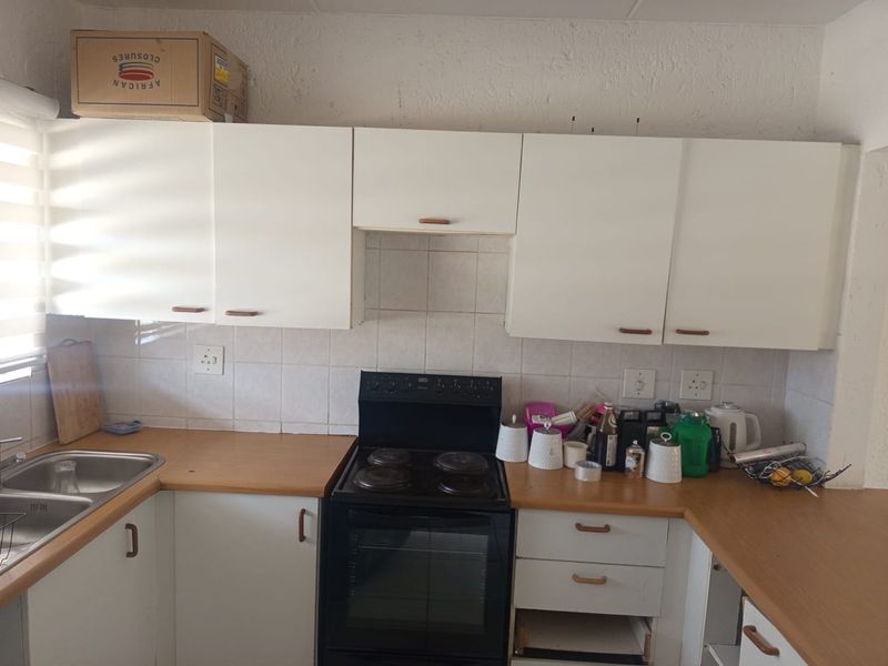 A functional kitchen featuring laminate countertops, white cabinetry, a tiled backsplash, and a freestanding stove, requiring minor repairs and cosmetic updates.