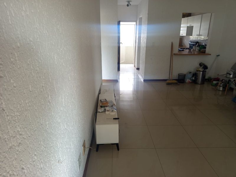 An open-plan living area featuring tiled flooring, textured walls, and a pass-through window connecting to the kitchen space.