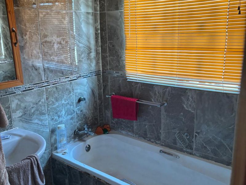 A functional bathroom featuring full-height marble-effect wall tiling, a built-in bathtub, and a wall-mounted basin.