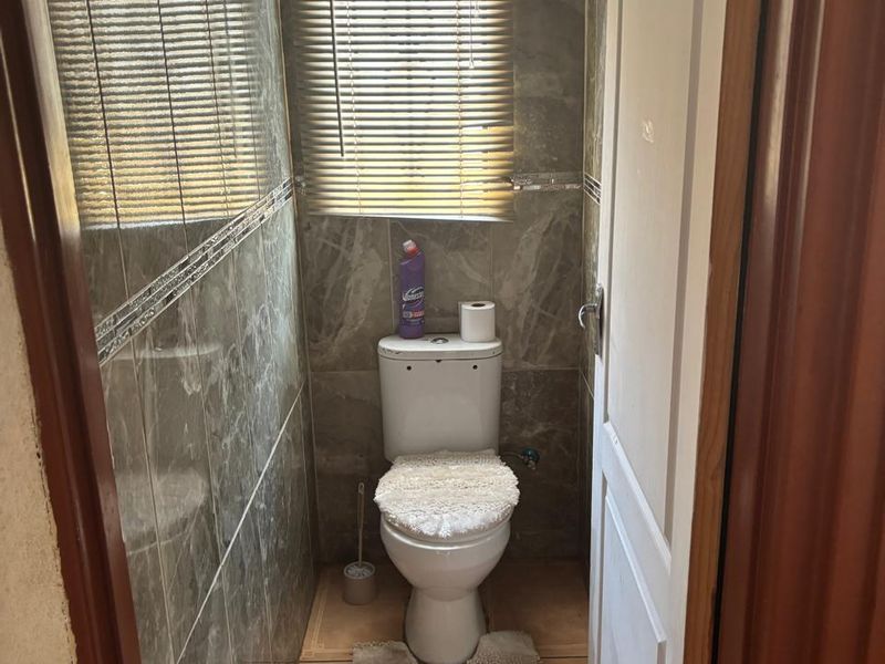 A compact guest bathroom featuring full-height marble-effect wall tiling, floor tiles, and a window with fitted venetian blinds.