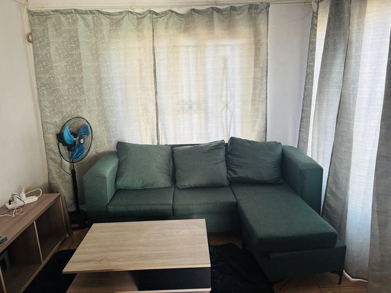 A compact living room area featuring tiled flooring and window treatments, currently showing signs of wear and needing cosmetic updates.