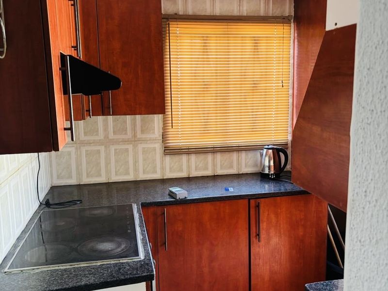 A compact kitchen featuring wood-look cabinetry, dark laminate countertops, an integrated electric hob, and tiled flooring with a neutral backsplash.
