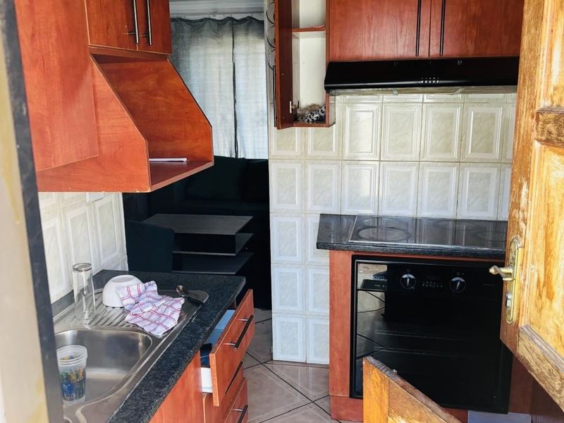 Compact kitchen featuring wood-tone cabinetry, integrated oven and hob, tiled backsplash, and tiled flooring, offering a functional layout for meal preparation.