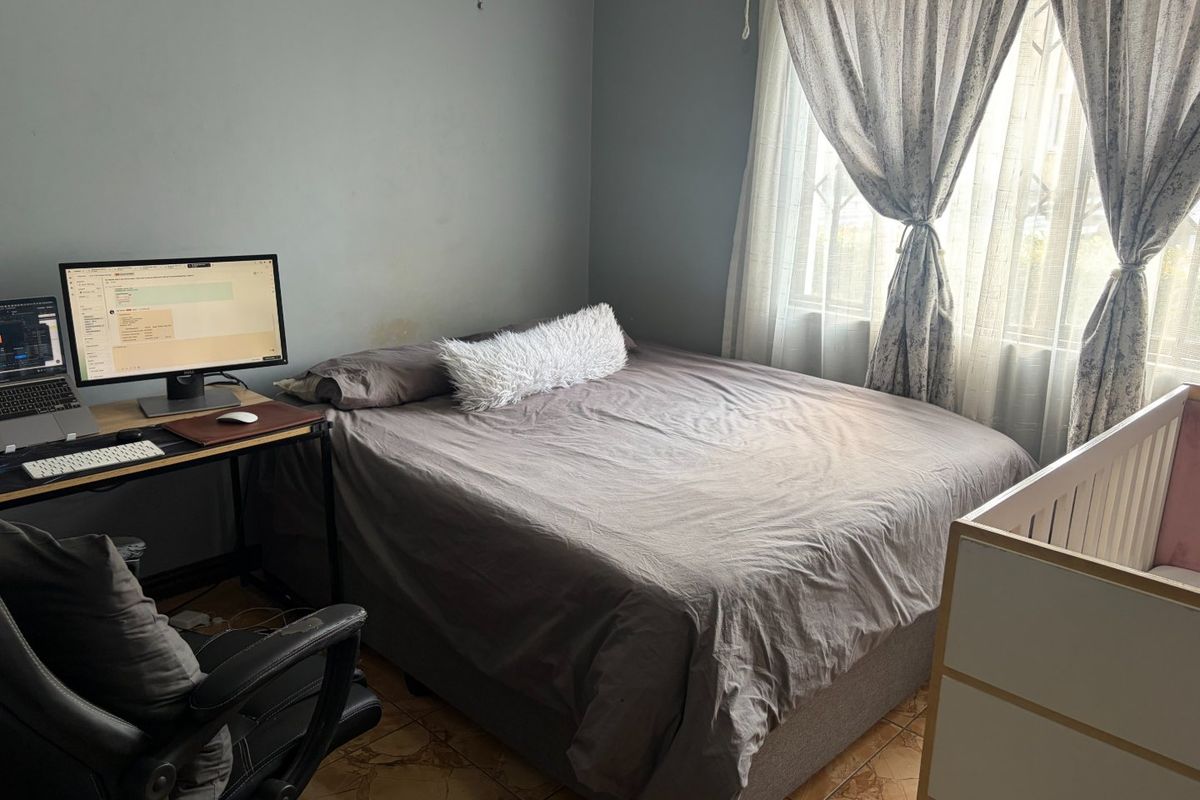 A functional bedroom featuring tiled flooring and natural light through window curtains, providing a versatile space for rest and work.