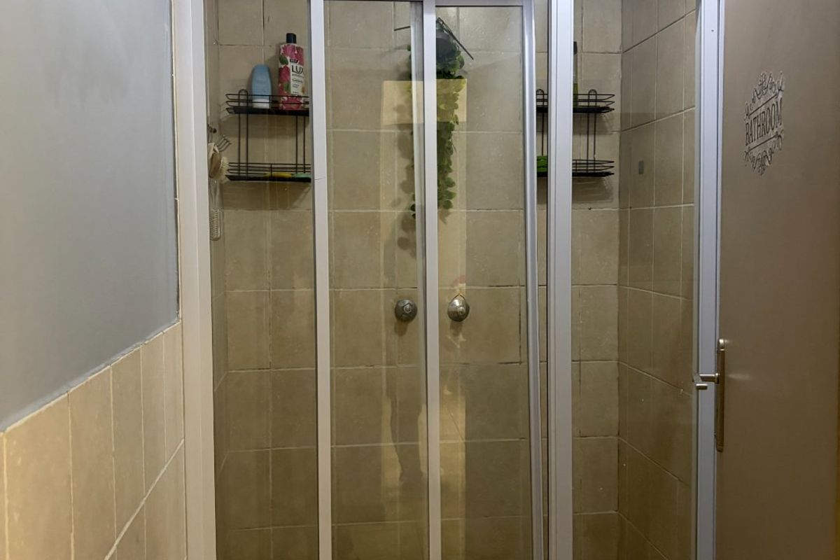 A functional bathroom shower enclosure featuring tiled walls and floor with a sliding glass door, showing signs of age and wear.