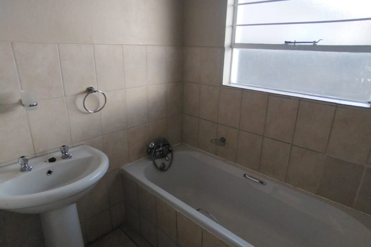A functional bathroom featuring a pedestal basin, built-in bathtub, and neutral wall and floor tiling. Requires minor maintenance to fixtures.