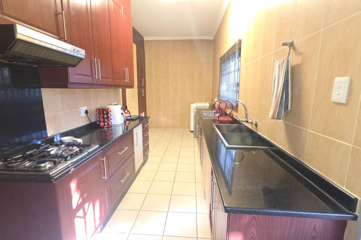 A functional kitchen featuring dark wood cabinetry, granite countertops, a gas hob with extractor fan, and tiled finishes throughout.