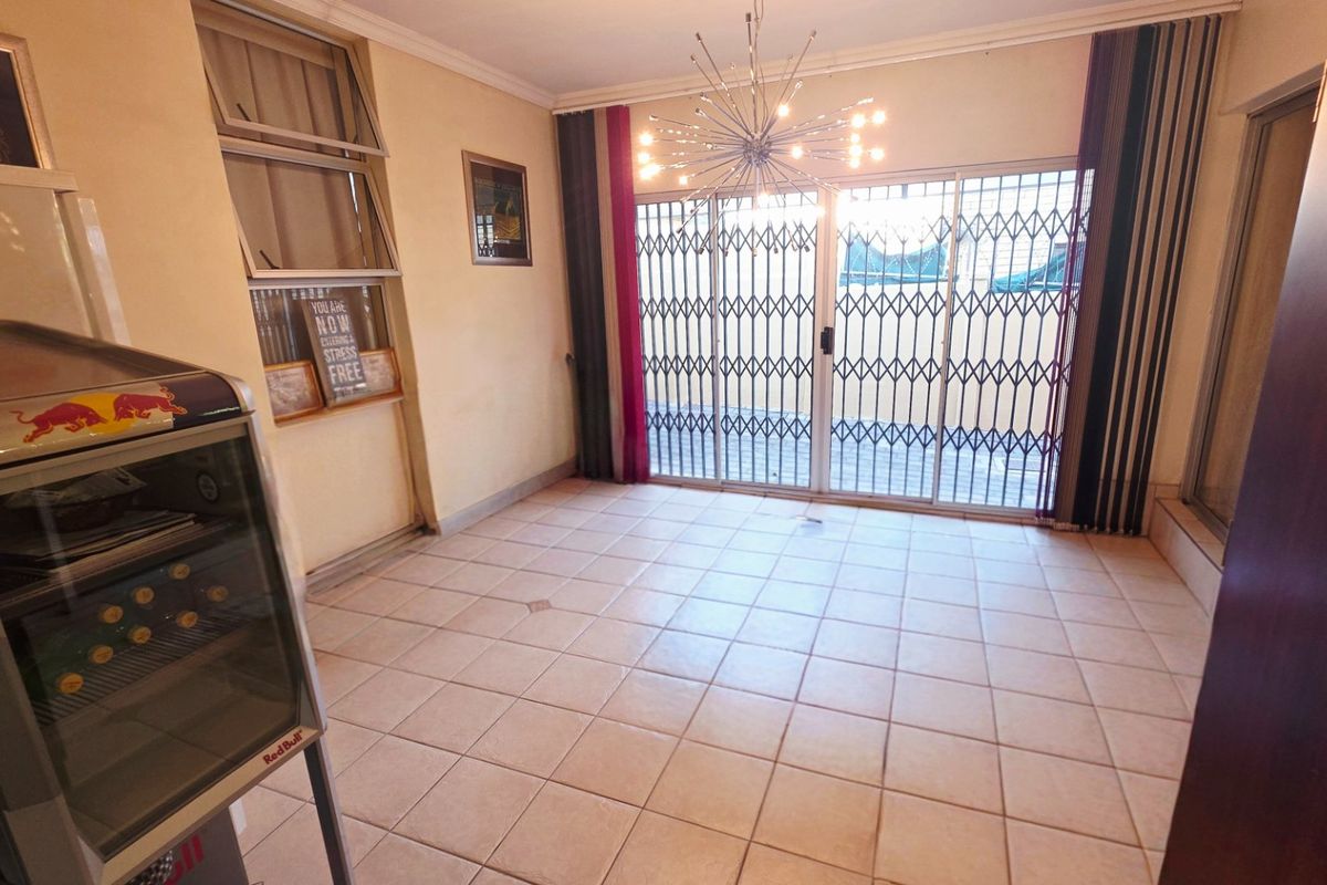 A bright, tiled living area featuring a modern chandelier, large sliding glass doors with security gates, and access to an outdoor space.
