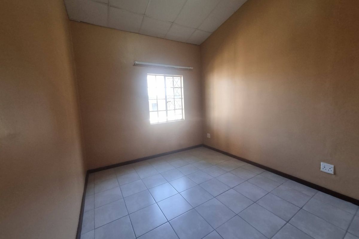 An empty bedroom featuring tiled flooring, a window with security bars, and a drop ceiling, offering a blank canvas for renovation.