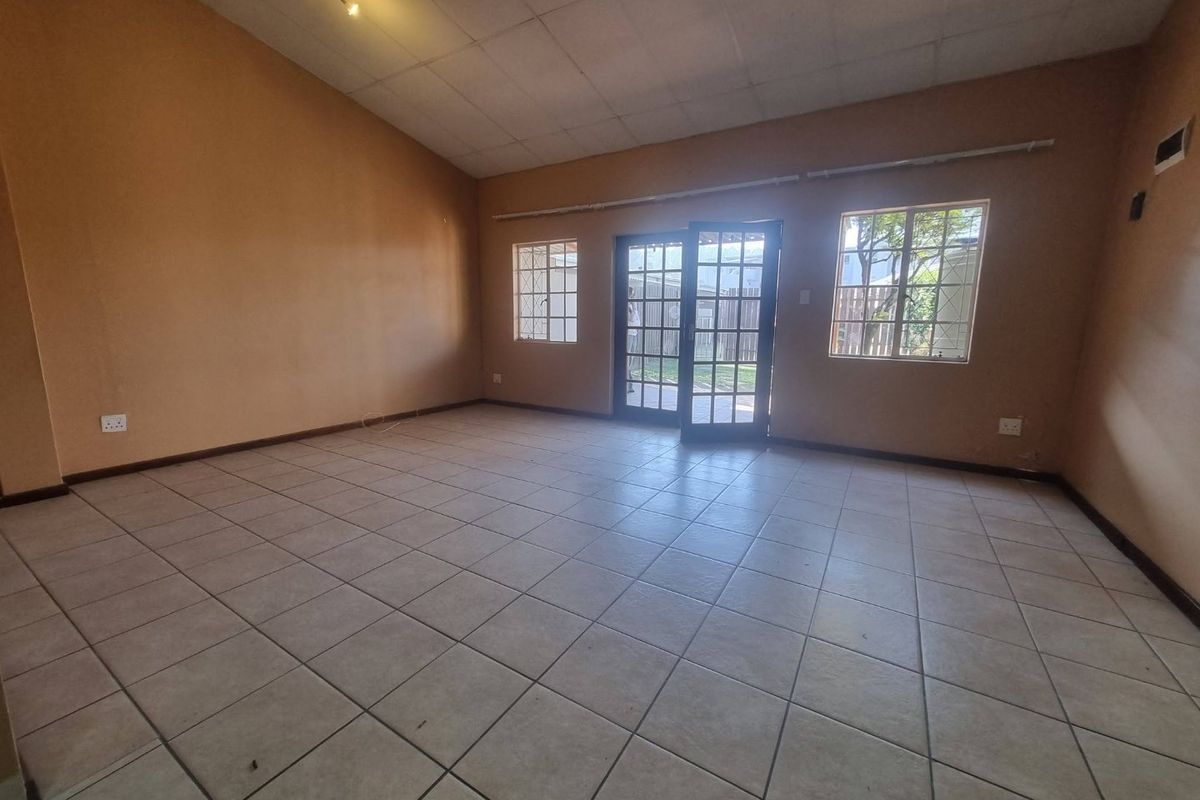 Spacious, empty living area featuring tiled flooring, drop ceiling tiles, and french doors providing direct access to the rear garden.