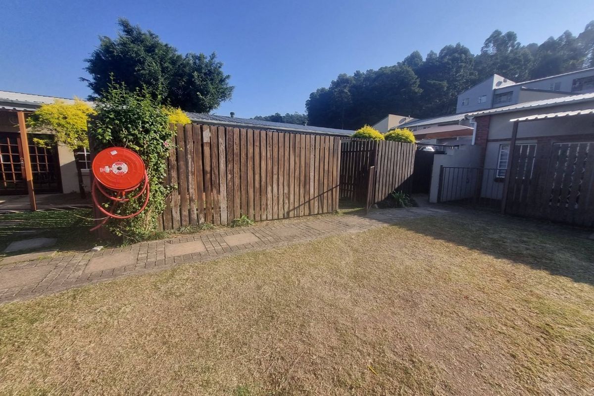 A rear garden area featuring a paved walkway, lawn, and timber boundary fencing with an attached fire hose reel.