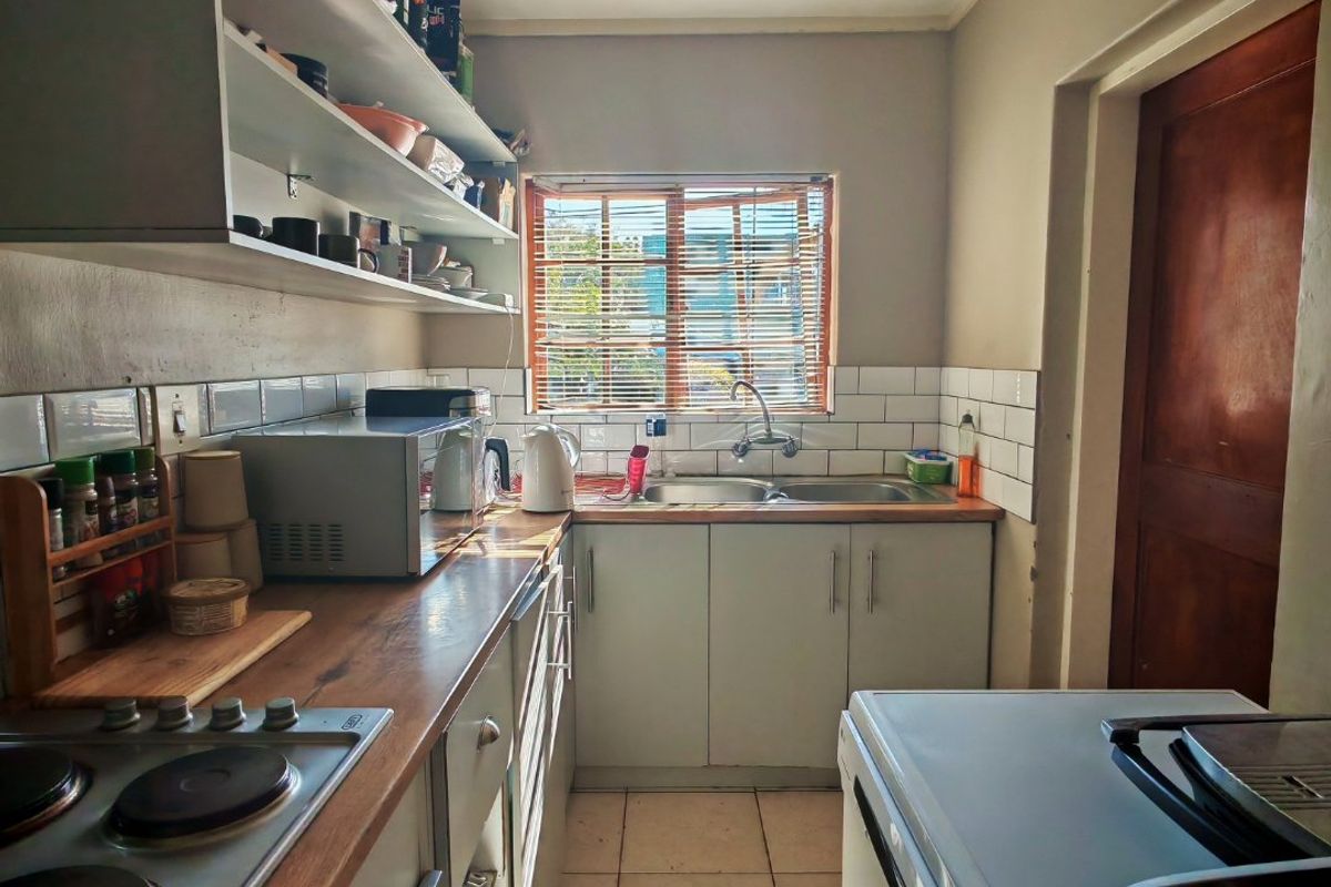 A functional galley-style kitchen featuring laminate countertops, built-in cabinetry, open shelving, and a tiled backsplash with a stainless steel sink.
