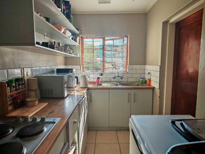 A functional galley-style kitchen featuring laminate countertops, built-in cabinetry, open shelving, and a tiled backsplash with a stainless steel sink.