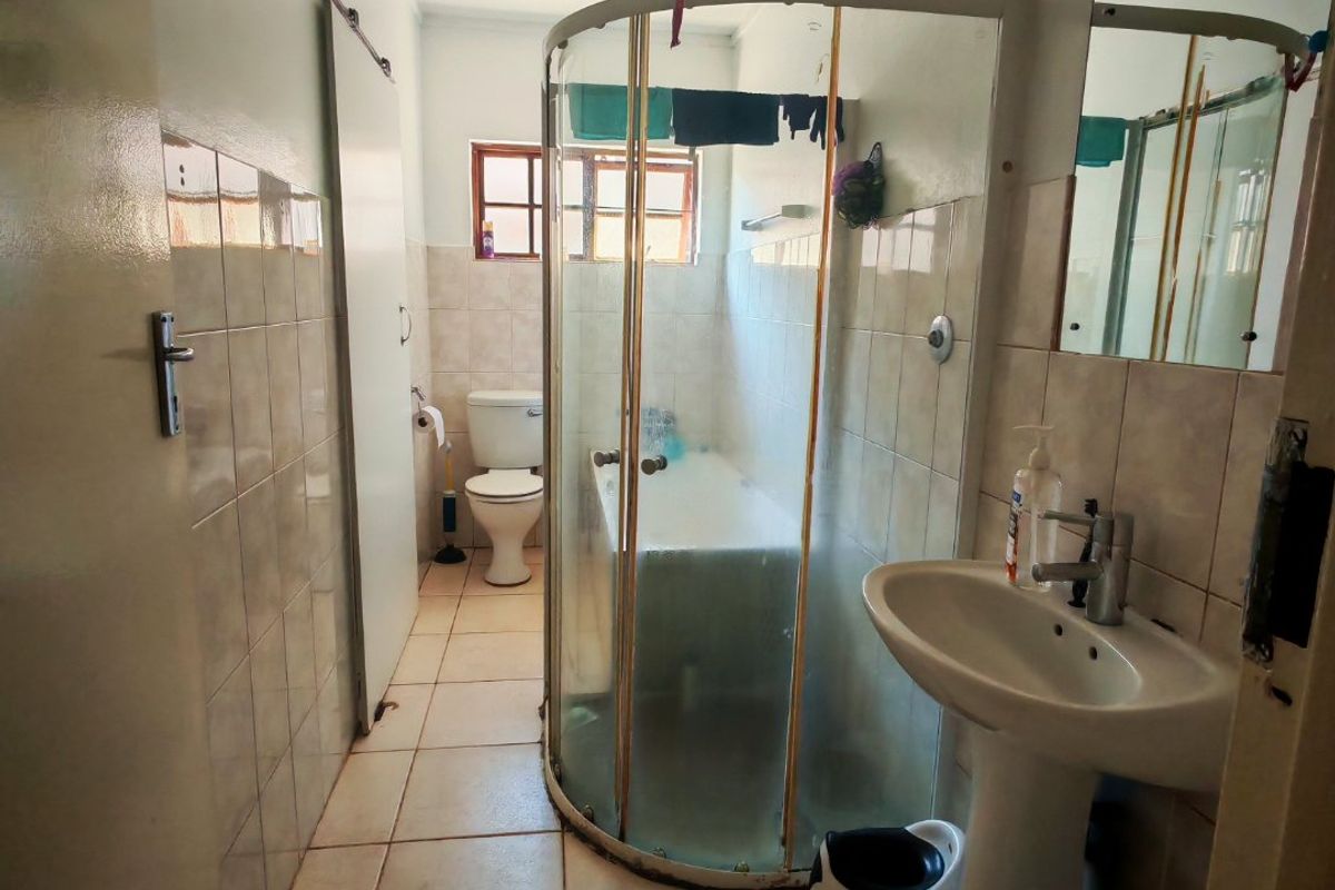 A functional bathroom featuring a pedestal basin, a corner shower enclosure, and a toilet, finished with tiled walls and flooring.