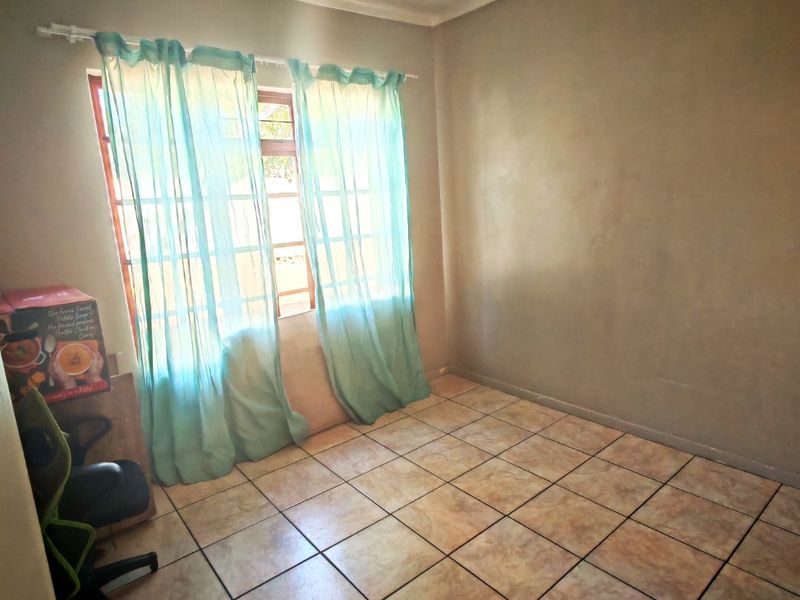 A vacant bedroom featuring tiled flooring and a window with security bars, offering a neutral space ready for personalization.