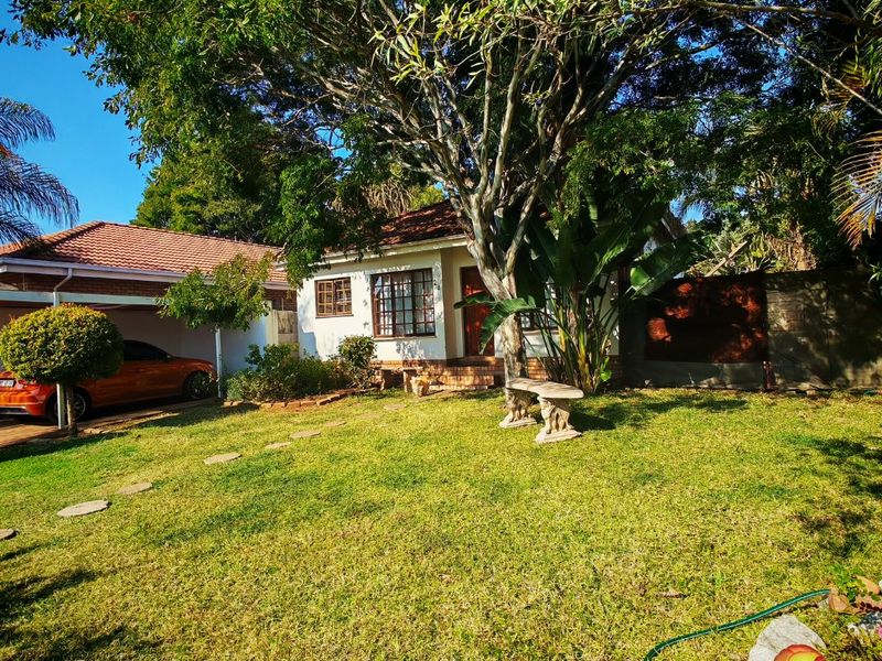 Front view of a residential house featuring a tiled roof, attached carport, and a well-maintained garden area with mature trees.