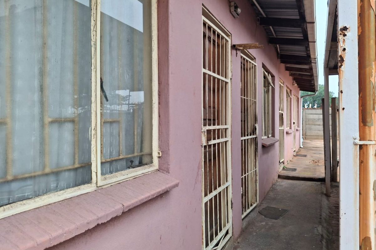 Side exterior walkway featuring metal security gates, weathered window frames, and a corrugated metal roof overhang showing signs of wear and corrosion.