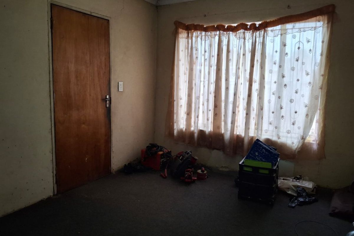 A vacant bedroom featuring a timber door and a large window, requiring cosmetic updates to the walls and flooring to improve its overall condition.