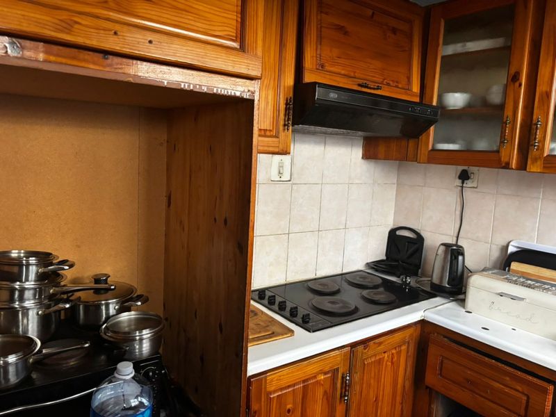 A dated kitchen featuring wooden cabinetry, a built-in electric hob, and an extractor fan with tiled splashback.