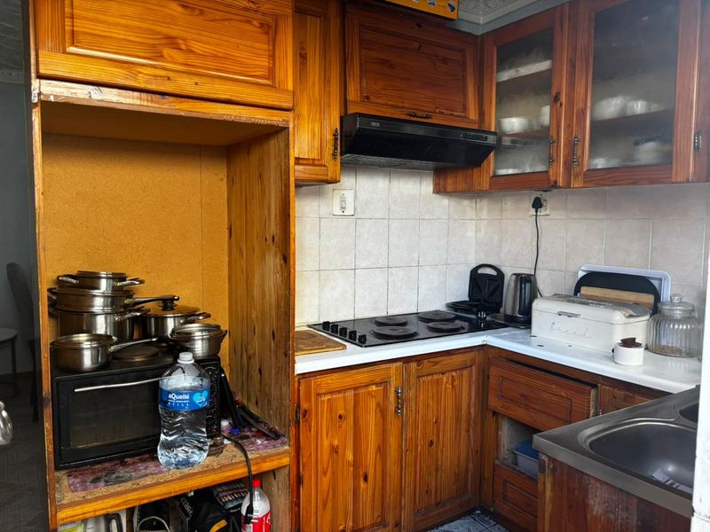 A compact kitchen featuring traditional wooden cabinetry, an electric hob with extractor fan, tiled backsplash, and a stainless steel sink.