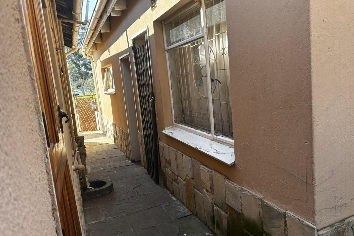 A narrow side passage featuring stone cladding, security gates, and paved flooring, showing signs of exterior wear and weathering.