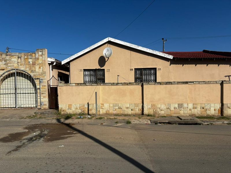 Front exterior view of a single-story house featuring a stone-clad boundary wall, security gates, and window bars.