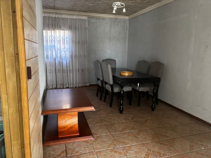 A dining room featuring tiled flooring, decorative ceiling tiles, and a security gate on the window, offering a functional space for meals.