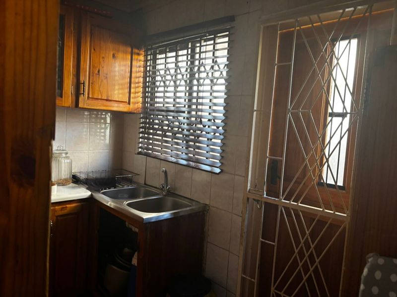 A compact kitchen featuring wooden cabinetry, a double bowl stainless steel sink, tiled splashbacks, and a secure metal gate leading to the exterior.