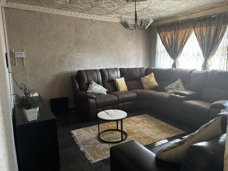 A living room featuring decorative ceiling tiles, coving, and tiled flooring, offering a dated aesthetic that could benefit from modern updates.